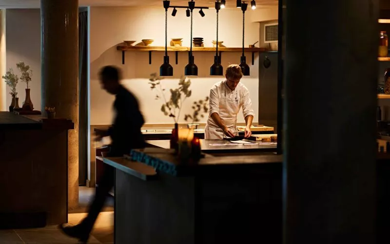 The interior of restaurant St. Barts, a view of the open kitchen with stainless steel counter tops, a chef in chefs whites prepares food.