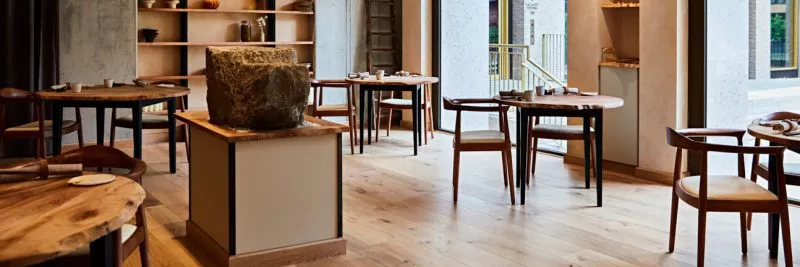 The interior of restaurant St. Barts, a line of wooden tables laid for services in a room with natural tones and wooden floors.