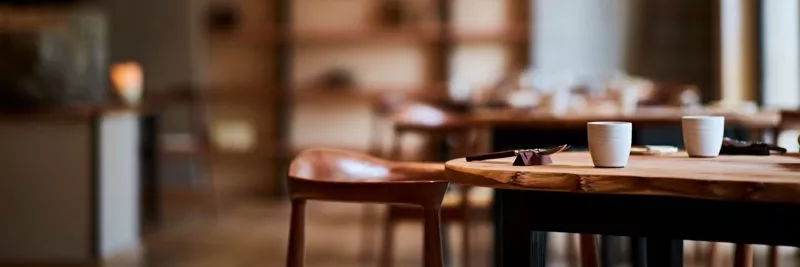 Interior image of restaurant St. Barts, foreground: a table laid with cups and cutlery, background: soft out of focus dinning room