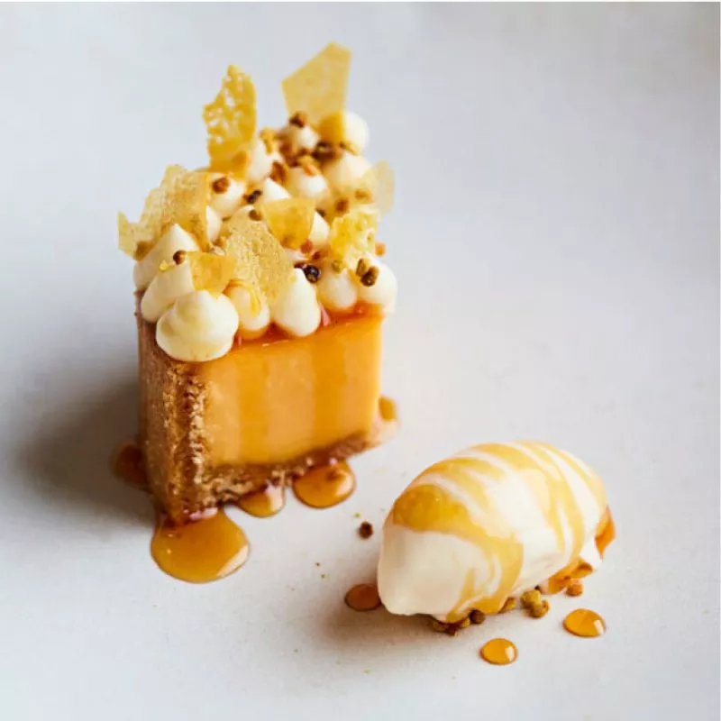 Close up of a desert at Restaurat St. Barts, a small cut of lemon tart topped with pipped cream and fine tuiles, a quenelle of ice cream on the side and a honey glaze.